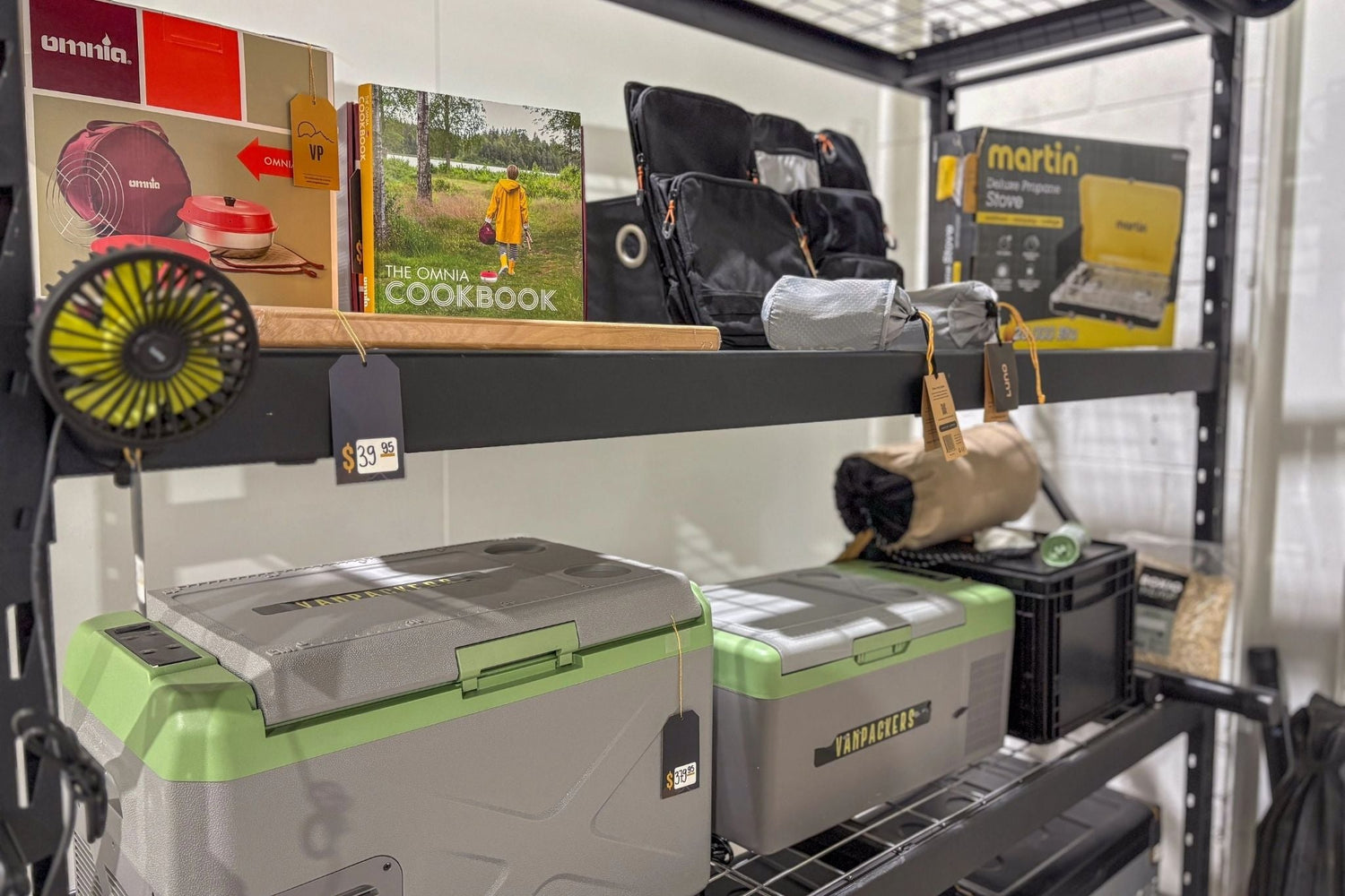 Camping gear rack with Martin stove, Vanpackers coolers, Luno accessories, portable fan and Omnia recipe book - everything you need for a well-equipped roadtrip.
