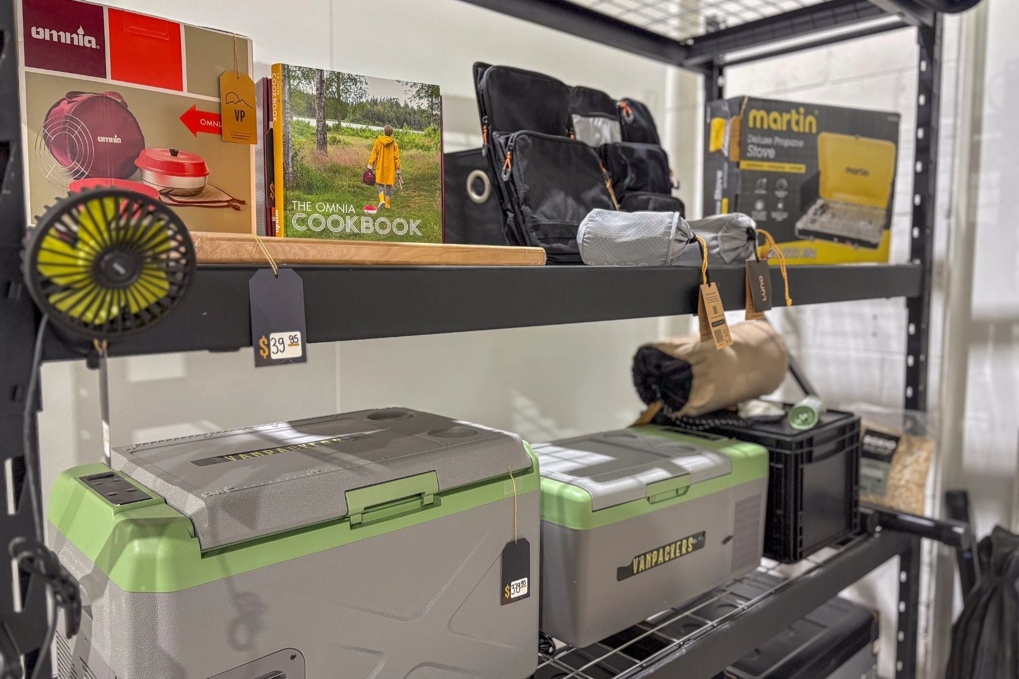 Camping gear rack with Martin stove, Vanpackers coolers, Luno accessories, portable fan and Omnia recipe book - everything you need for a well-equipped roadtrip.