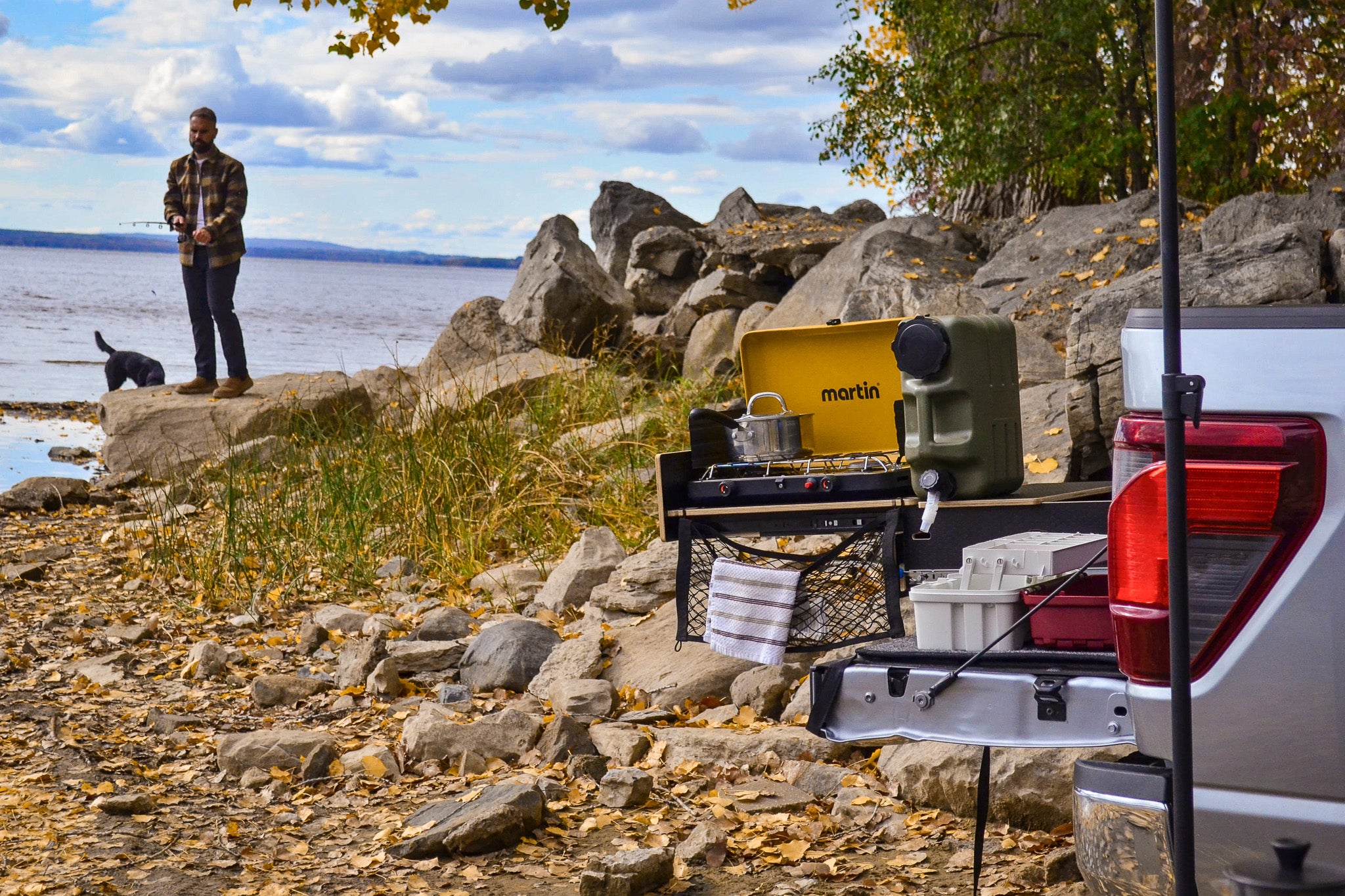 Person standing by a lake with a truck bed setup featuring a Martin brand cooler.